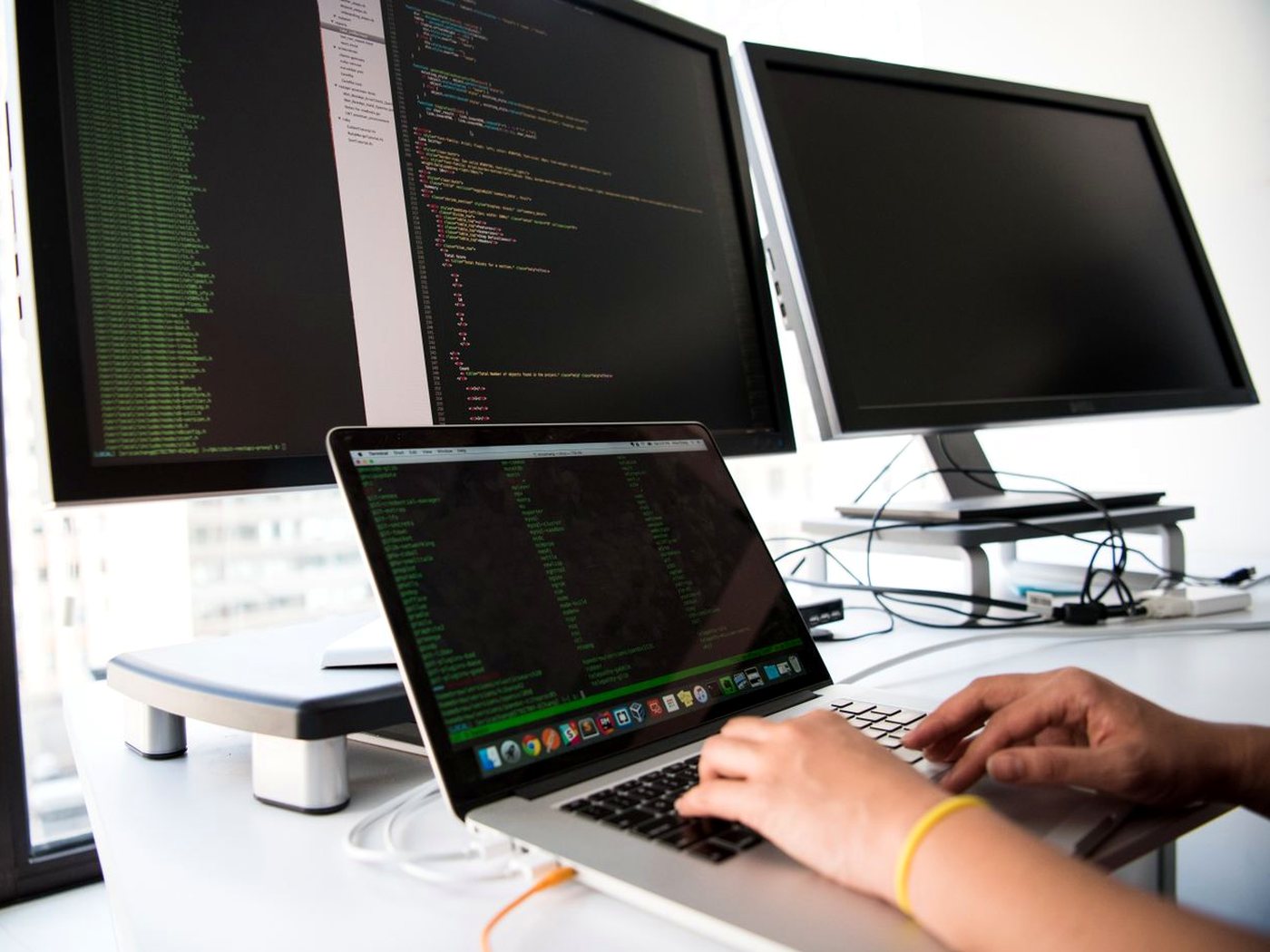 Des écrans remplis de lignes de code et des mains sur le clavier d’un ordinateur portable