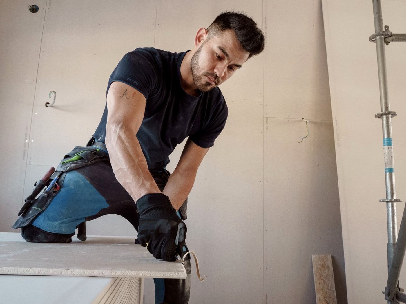 Un plaquiste découpe une plaque de plâtre sur un chantier