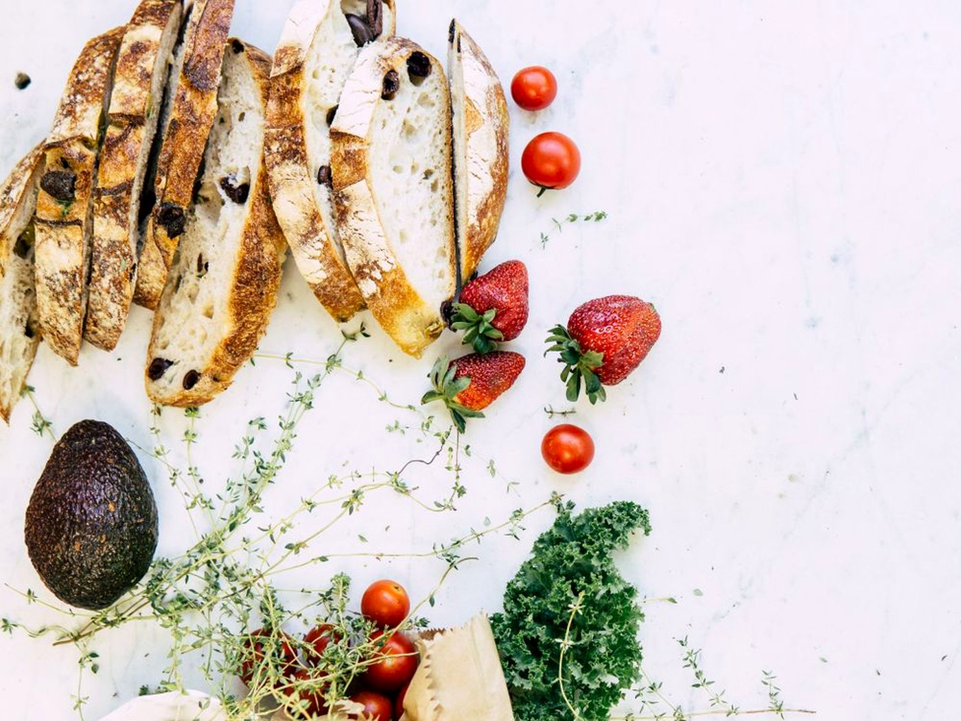 Des tranches de pain aux olives sur un marbre clair, avec des fraises et des tomates cerises