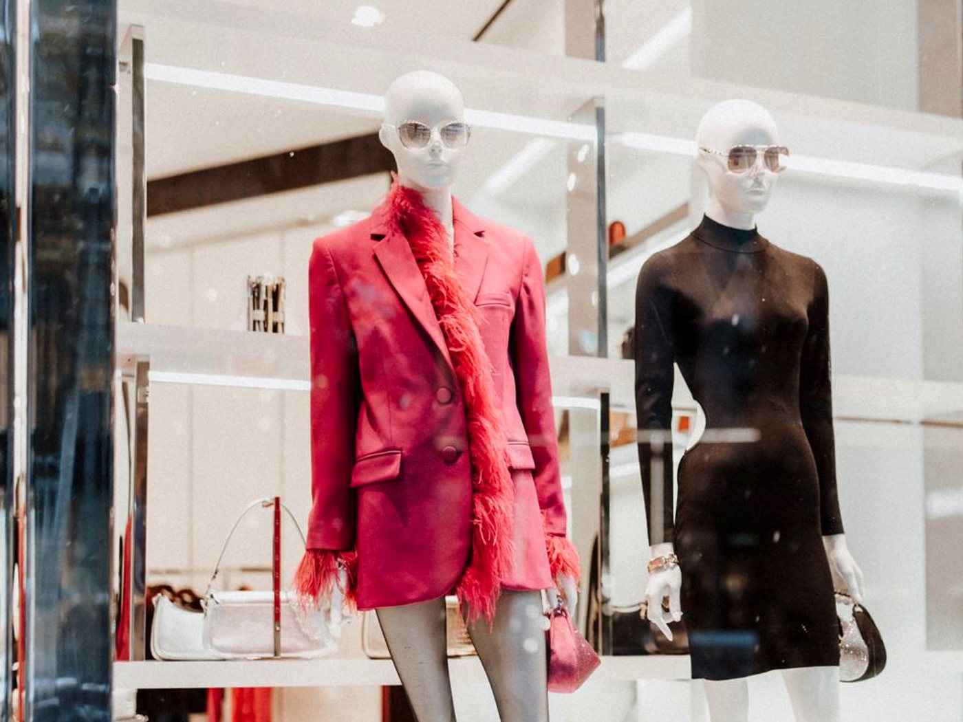 Deux mannequins en vitrine, l’un en veste rouge bordée de plumes, l’autre en robe noire