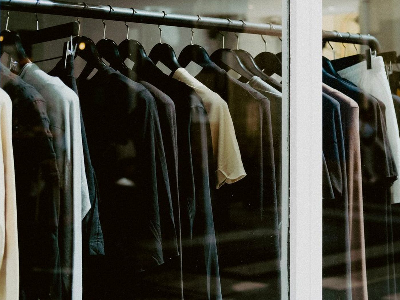 Des vêtements sur cintres, vus à travers la vitrine d’une boutique