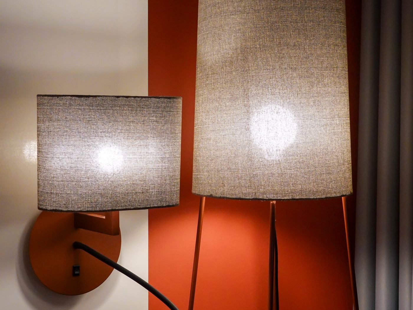 Une applique et un lampadaire allumés dans une chambre d’hôtel