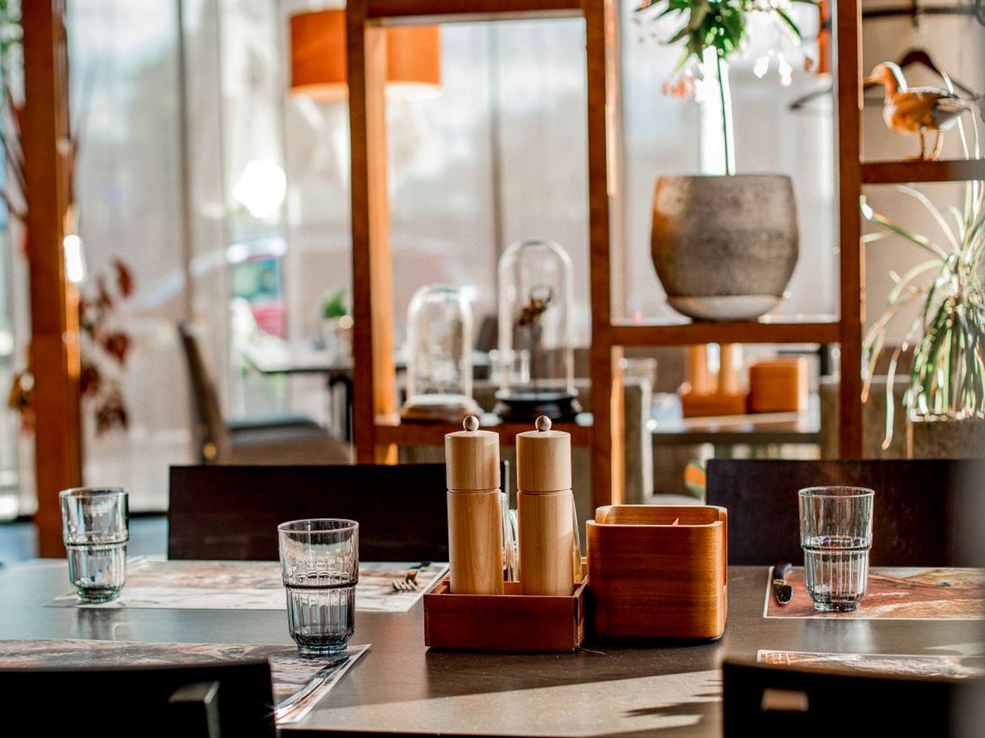 Une table de restaurant avec ses verres et ses moulins à sel et à poivre en bois, dans une salle baignée de lumière
