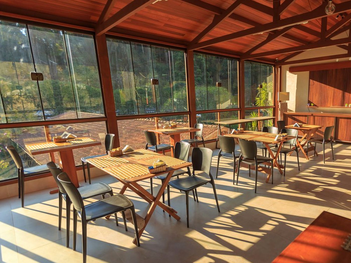 La salle vitrée d’un petit restaurant, tables en bois et chaises au soleil