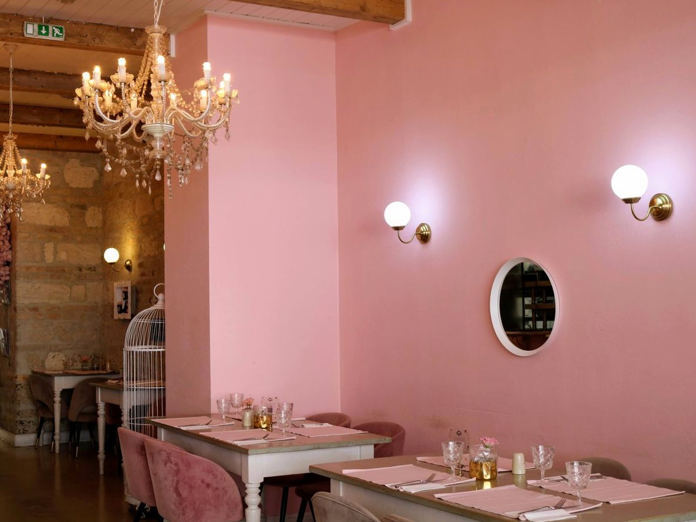Une petite salle de restaurant aux murs roses, tables dressées sous un lustre à pampilles