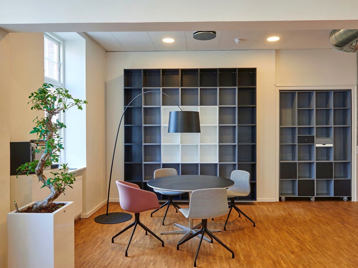 Un coin réunion dans des bureaux : table ronde, quatre sièges, lampadaire et bibliothèque murale