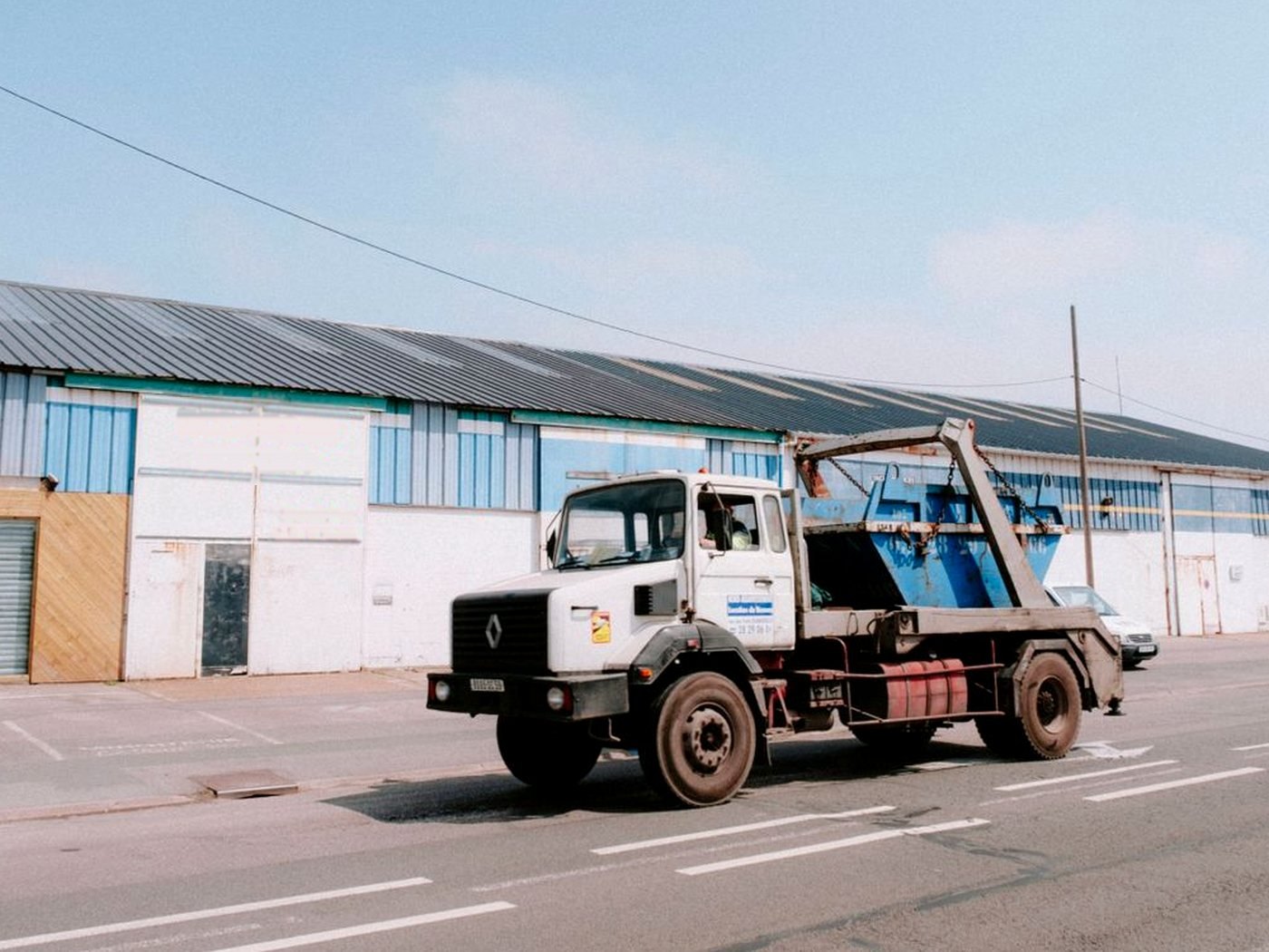 Un camion blanc chargé d’une benne bleue passe devant un hangar