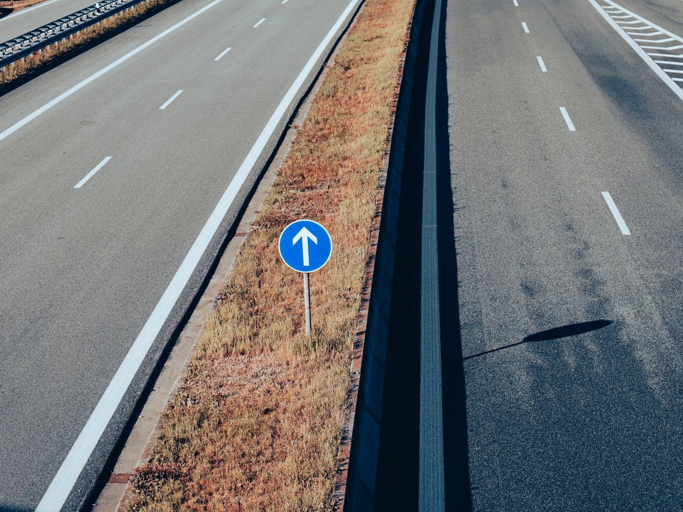 Une autoroute vide vue d’un pont, avec un panneau bleu à flèche blanche sur le terre-plein